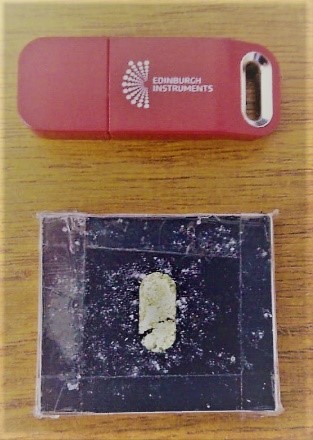 The diffuse reflection powder sample holder filled with Benzil powder (USB drive shown for size comparison). 