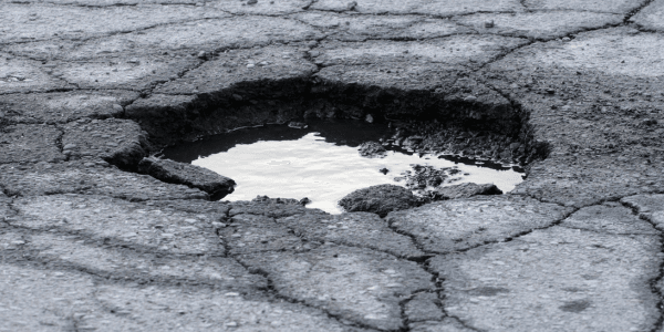 large pothole with cracked road around it 